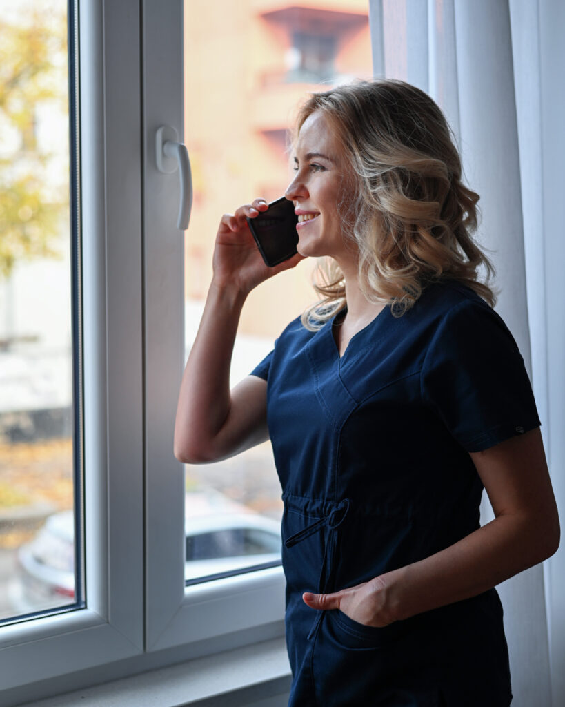 Alona, the business owner, gazing thoughtfully through a window, symbolizing contemplation and creativity in her massage and art business.